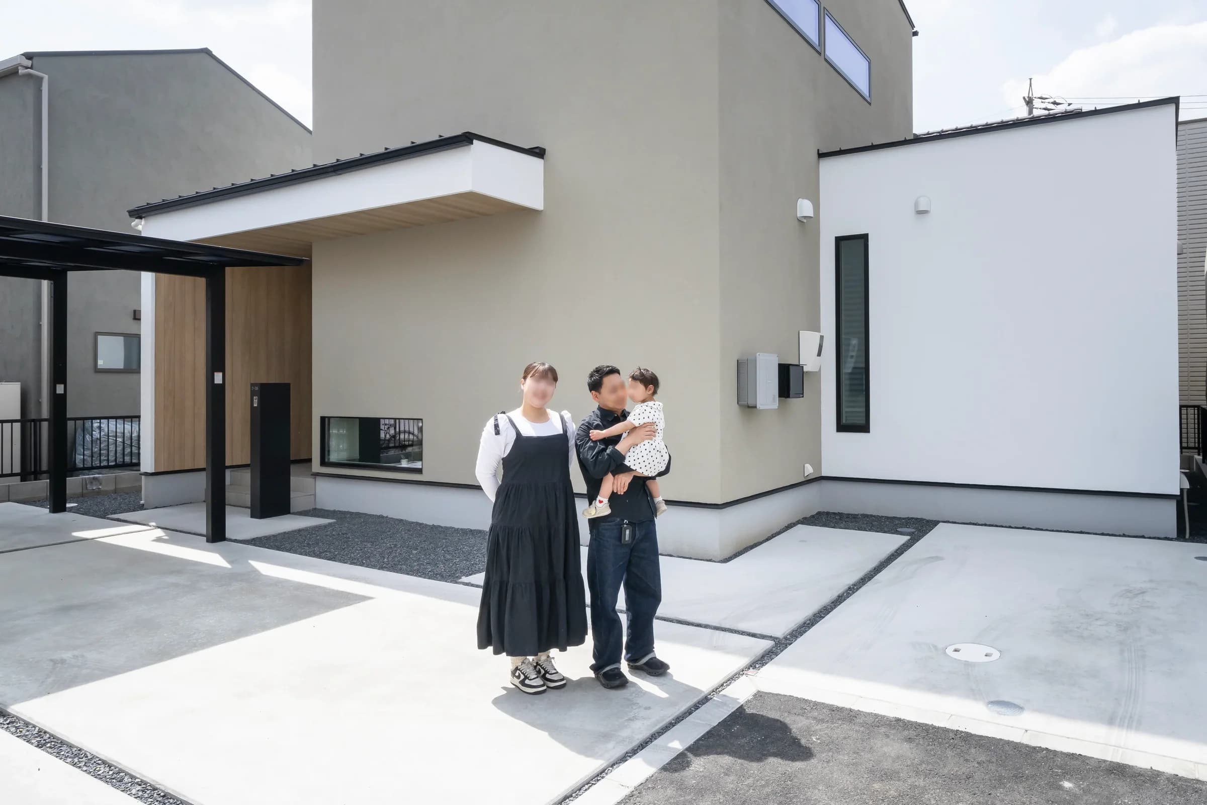 グレーの外壁の住宅の前に立つ家族3人